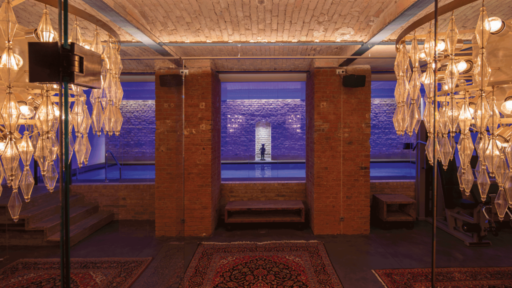 Moderner Pool in einem Untergeschoss mit altem Mauerwerk. Im Vordergrund hängen dekorative Kronleuchter.