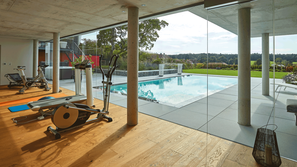 Fitnessbereich mit großer Glasfront und Blick auf den Pool und Garten.