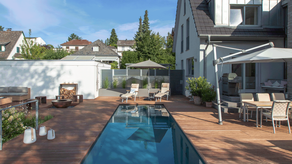 Pool mit großzügiger hölzerner Terrasse und mehreren Sitzmöglichkeiten.