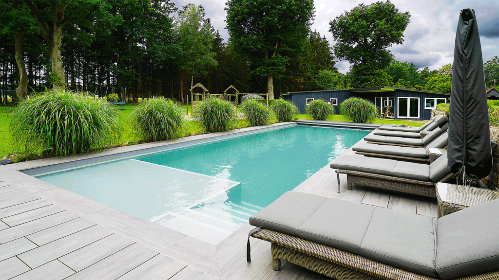 Pool mit Relax-Liegen. Blick in den sehr grünen Garten mit vielen hohen Bäumen.