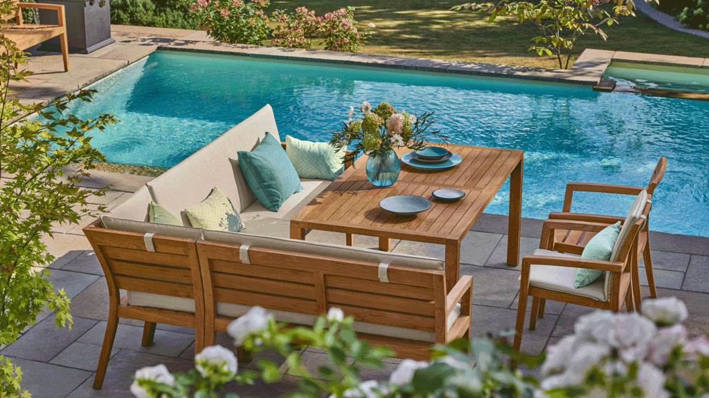 Gemütliche Eckbank, mit Tisch und zwei Stühlen aus Teakholz neben einem Pool. Ein Platz zum Teilen.