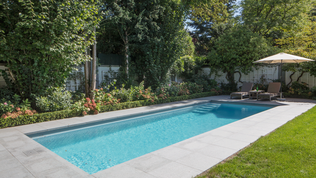 Pool in einem Garten mit einer Sitzecke auf der gefliesten Terrasse.