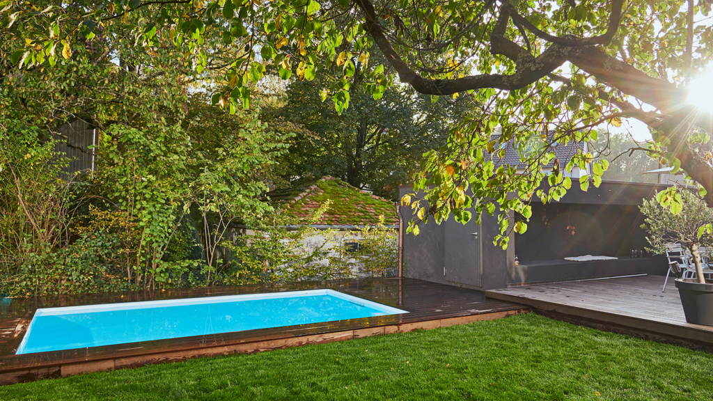 Kleiner Pool mit Holzterrasse im Garten eines Einfamilienhauses.