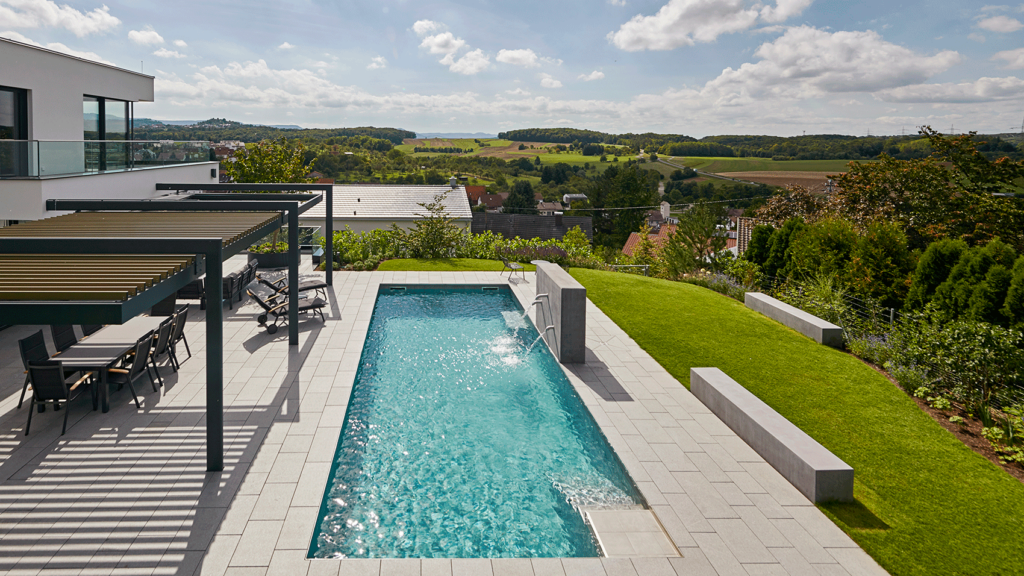 Blick aus der Vogelperspektive auf einen großen Pool, eingebettet in eine Terrasse mit Teilüberdachung und im Hintergrund Aussicht auf die Schwäbische Alb.