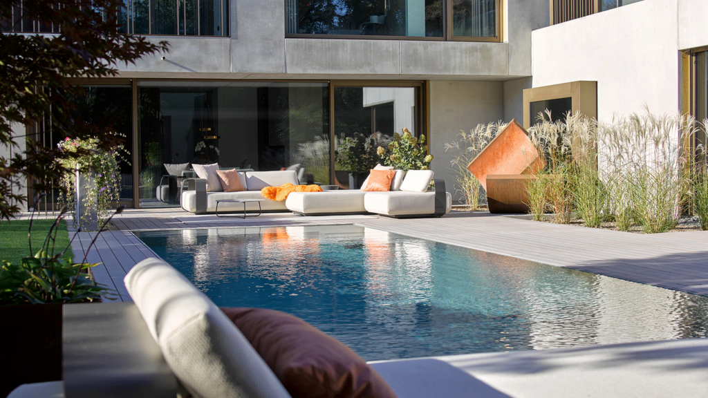 Ein Pool mit einer Holzterrasse und Loungemöbeln im Garten.