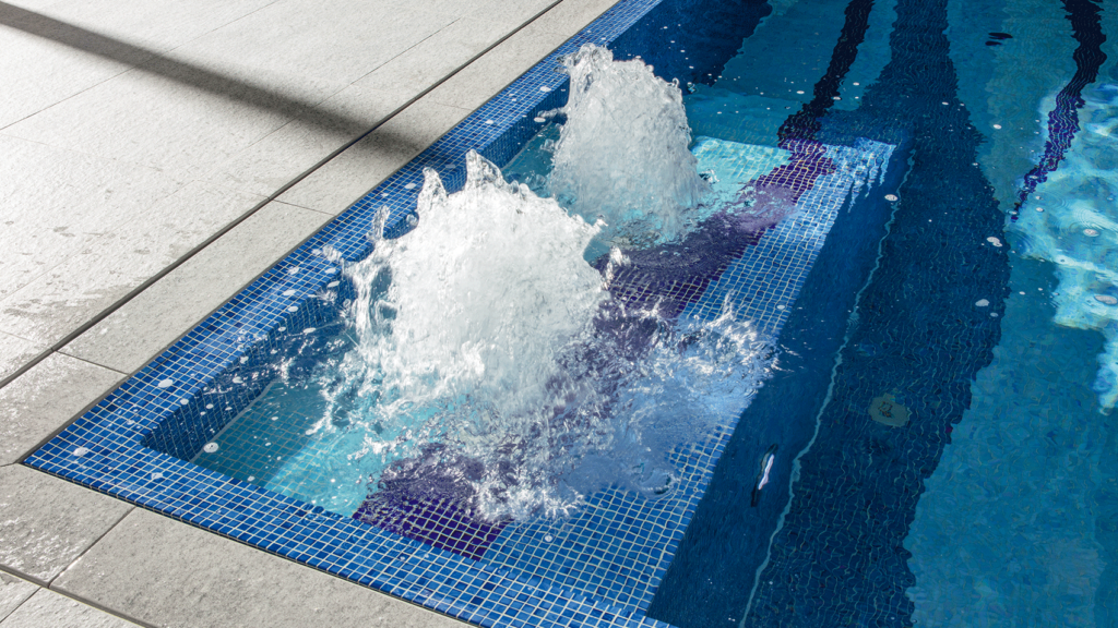 Detailansicht eines mit Mosaiksteinchen gefliesten Indoorpools. Zu sehen ist die Einstiegstreppe mit einer integrierten Luftsprudelplatte.