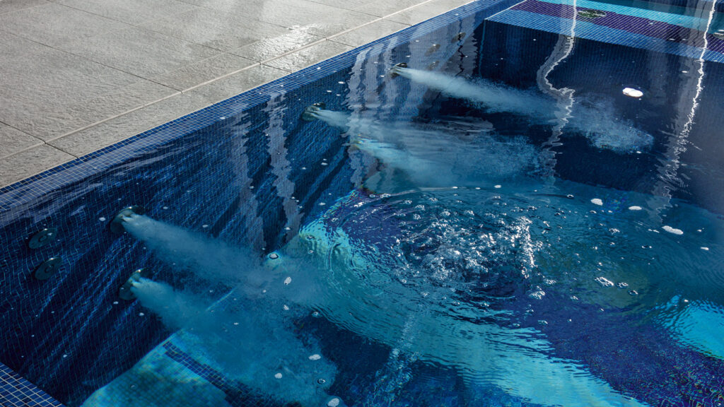 Detailansicht eines mit Mosaiksteinchen gefliesten Indoorpools. Zu sehen sind mehrere Massagedüsen in der Beckenwand.