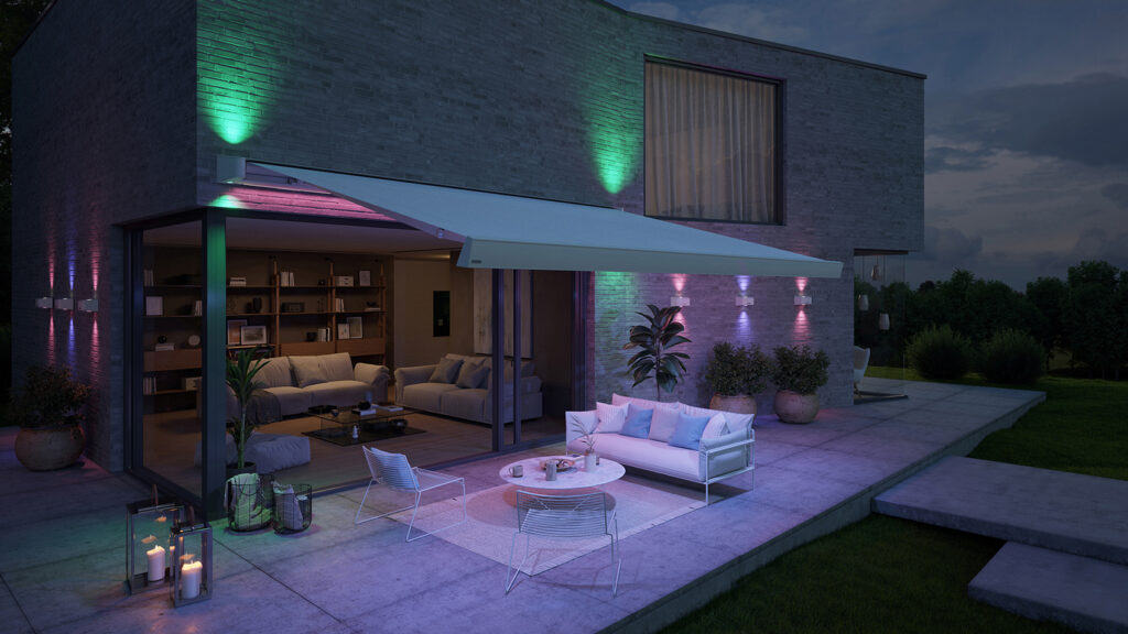 Blick auf eine Terrasse bei Nacht. Die Sitzgruppe wird von einer mit LED beleuchteten Markise überdacht und verbreitet eine gemütliche Lichtstimmung.