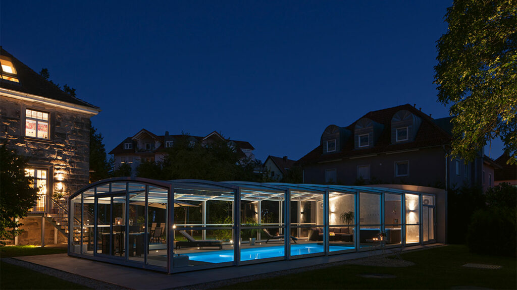 Pool mit Überdachung bei Dunkelheit. Das Haus im Hintergrund und der Pool sind beleuchtet.