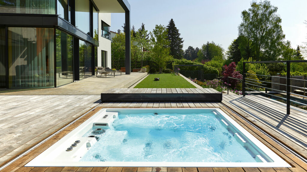 Modernen Wohnhaus mit großen Fenstern, daneben die Holzterrasse mit einem Whirlpool eingelassen.