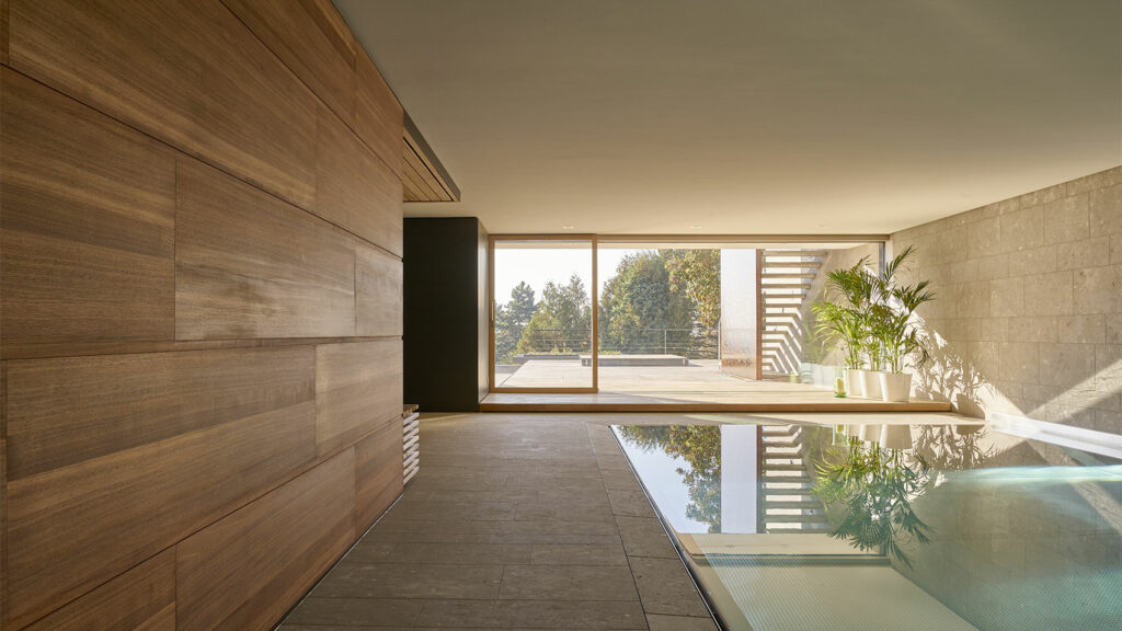 Schwimmhalle mit Holz- und grauen Natursteinwänden und großer Glasschiebetür zum Garten.
