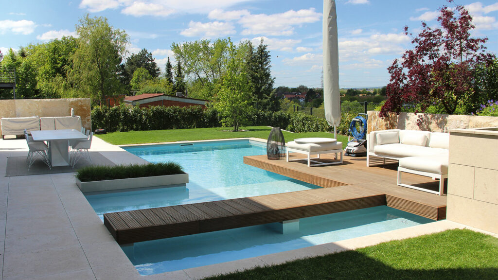 Pool mit Holzsteg, welcher zu einem Holzdeck mit gemütlicher Gartenlounge führt.